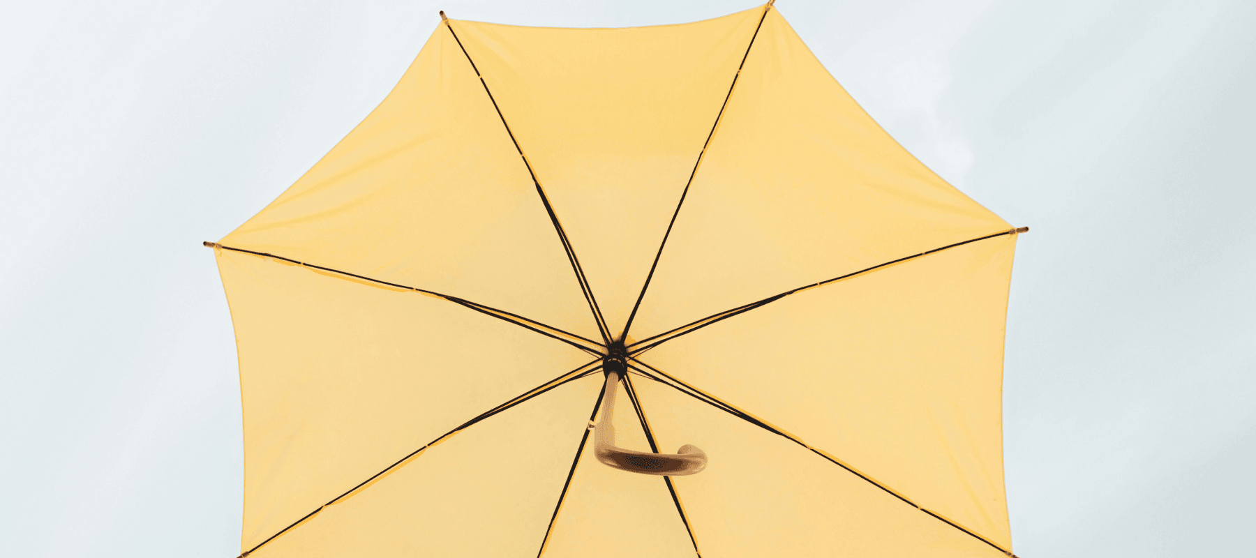 A low-angle view of a bright yellow umbrella against a pale sky, representing an integrated layer of AI for family office software.